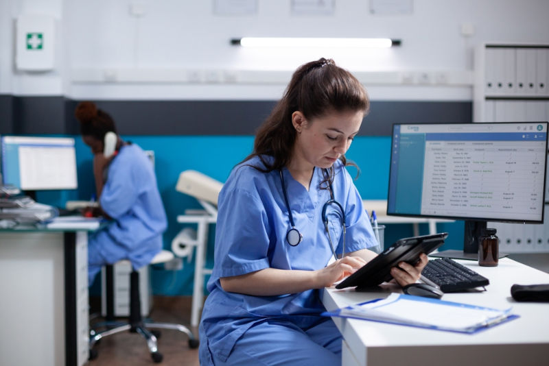 A tired nurse consulting a patient chart on a tablet