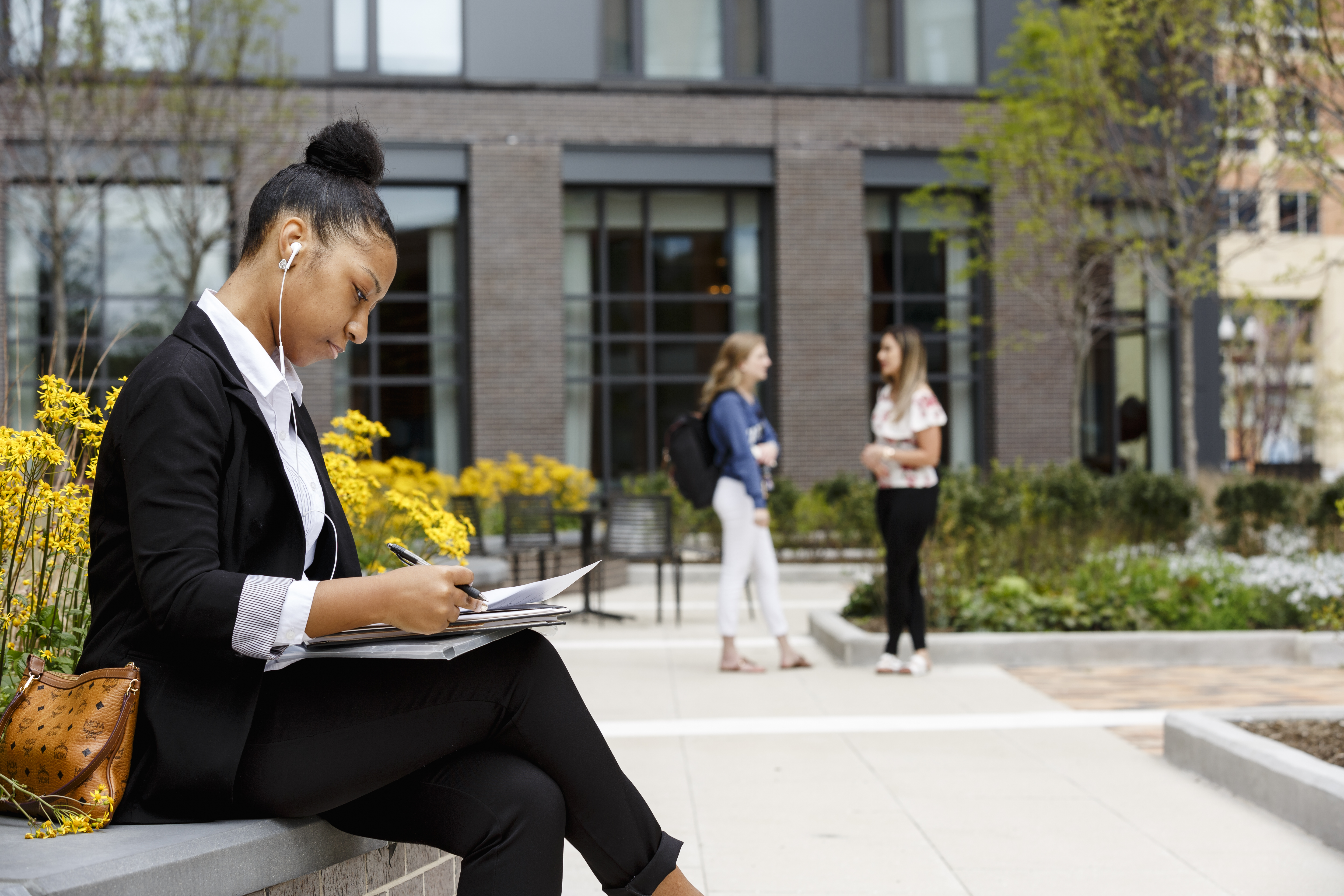 A student reviews papers while sitting in front of a university building.