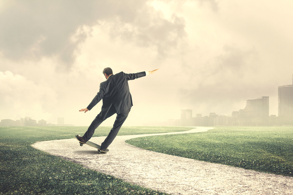 A person wearing a suit balances precariously on a skateboard.