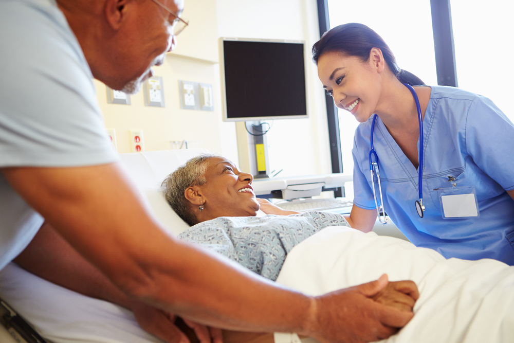 An RN working with her patient with husband looking on