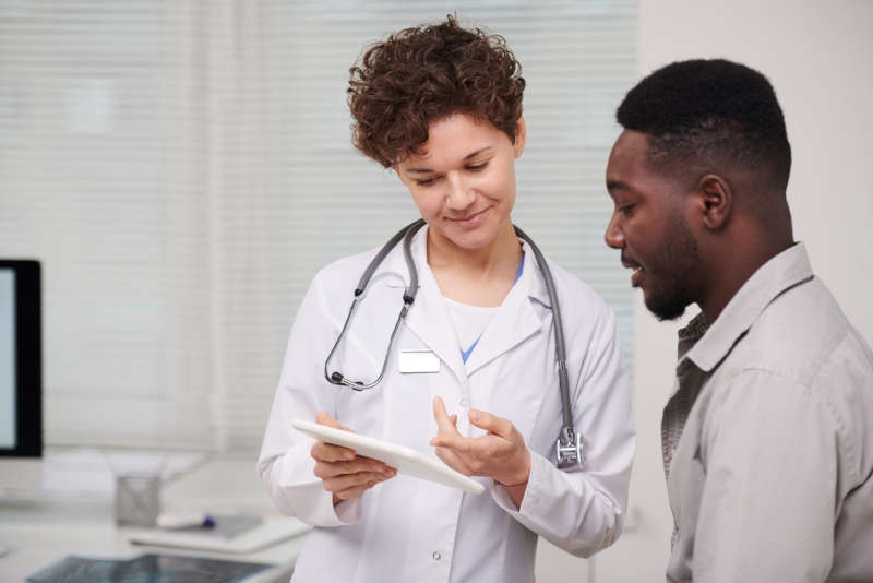 A nurse practitioner holding a tablet consults with a patient.